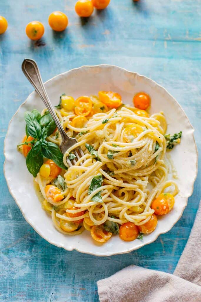 A bowl of spaghetti with sun gold tomatoes and basil on a blue background.
