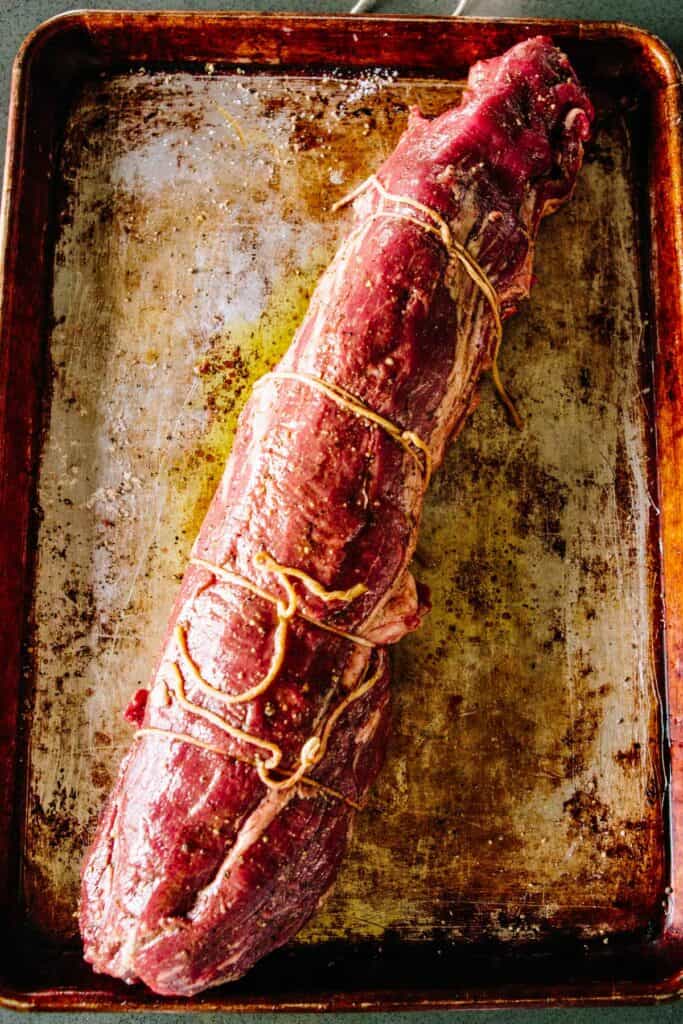 A raw, trimmed and tied beef tenderloin on a baking sheet.