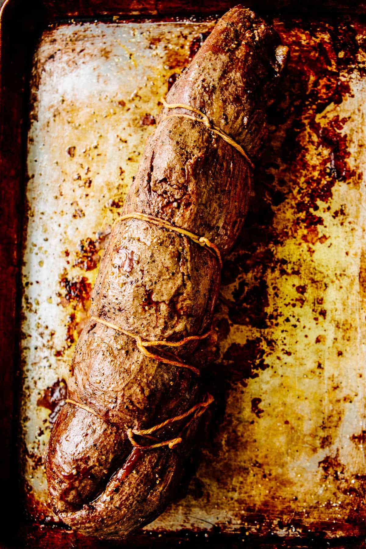 A tied and roasted loin of beef on a sheet pan.