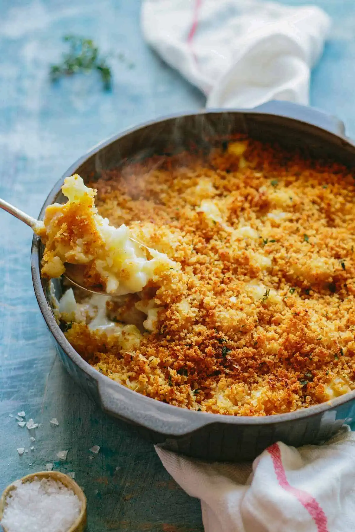 A spoon scooping out baked cauliflower with breadcrumbs from a casserole dish.