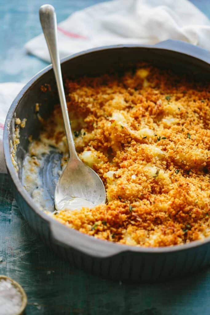 A close up of a dish of cauliflower au gratin with a spoon inside.