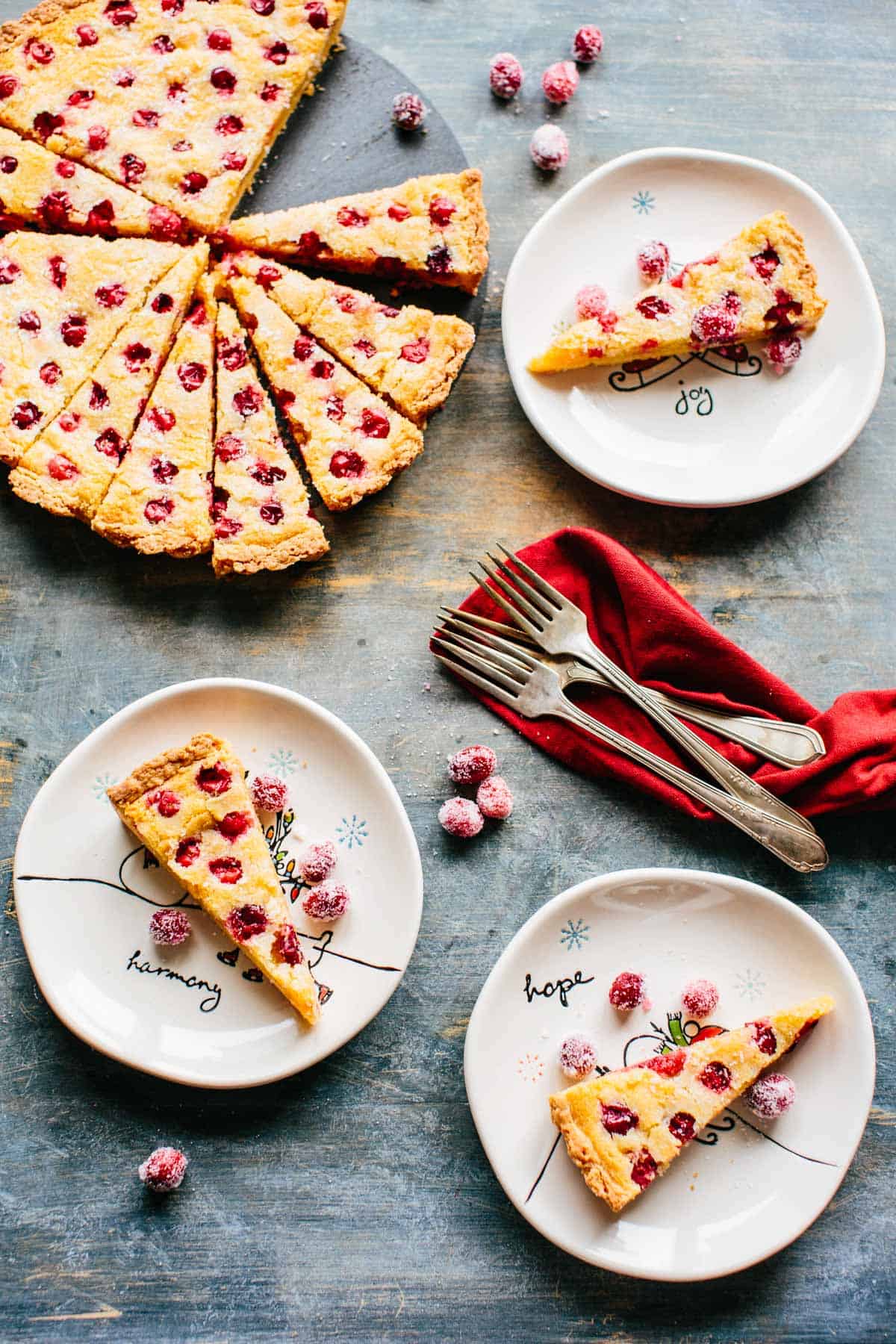 Birds eye view of several plates with slices of tart and a red napkin with silverware.