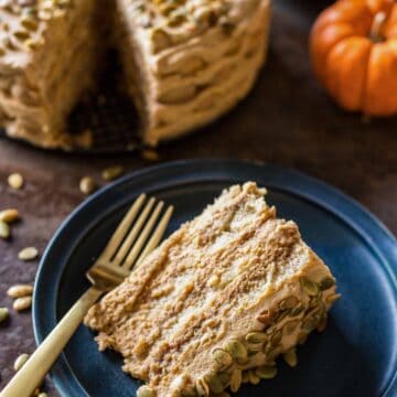 A slice of pumpkin tiramisu on a blue plate with the cake and pumpkins in the background.