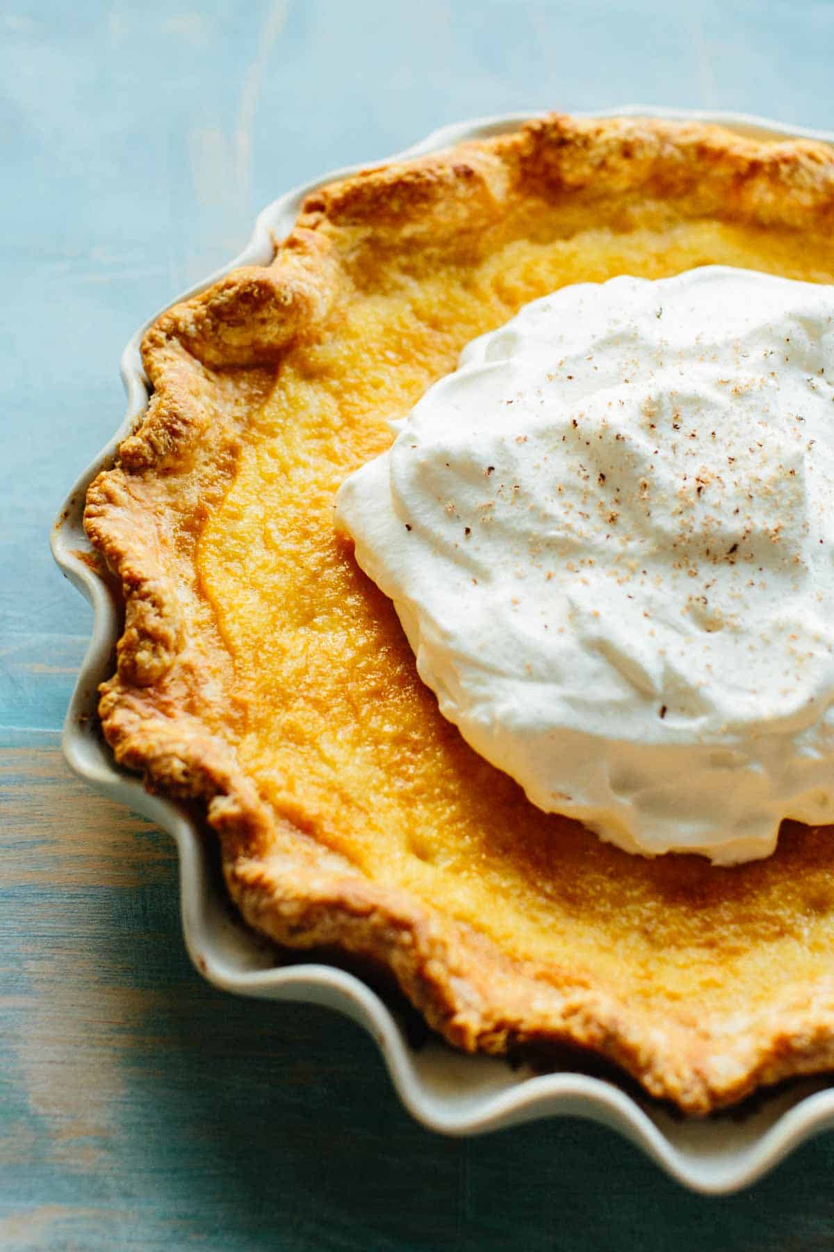 Side view of a custard pie with a big dollop of whipped cream on top.