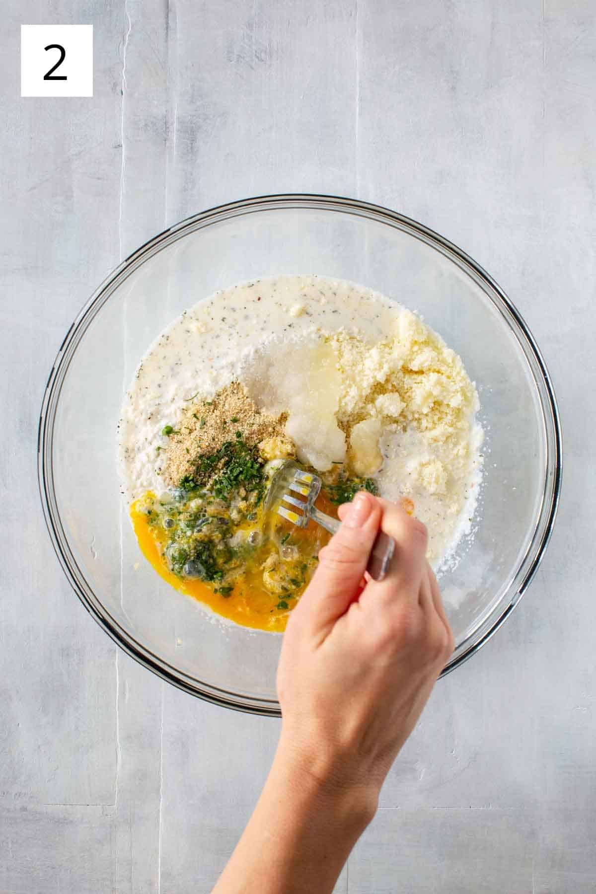 Mixing together breadcrumbs, salt, grated cheese, parsley, milk and eggs.