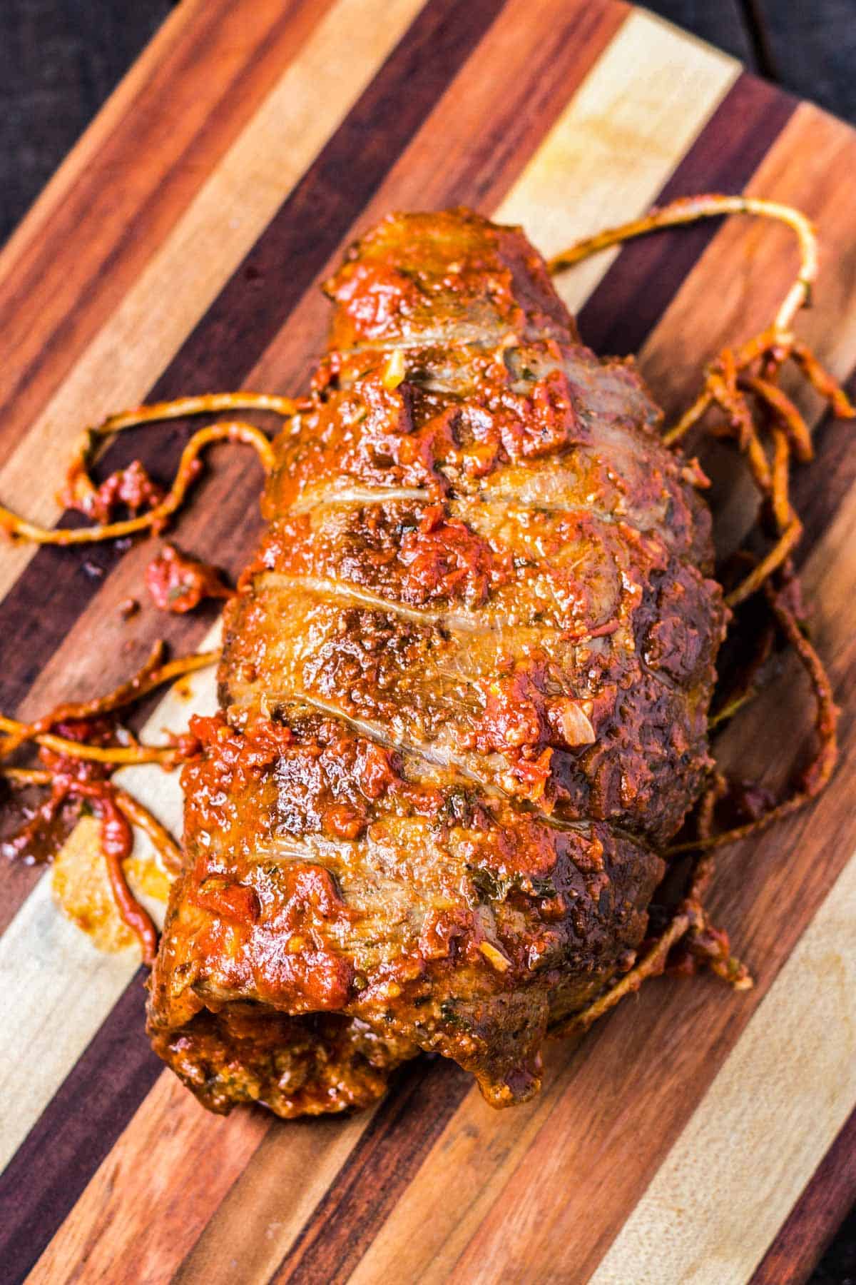 A whole braciole smothered in tomato sauce on a wood cutting board with butchers twine.