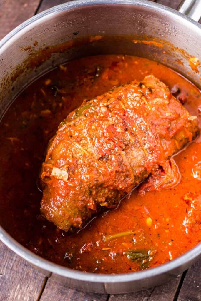 Overhead shot of a large piece of meat smothered in red sauce in a pot.