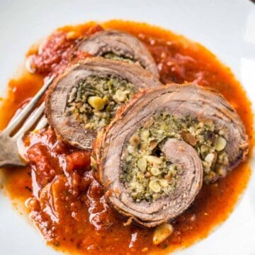 Close up of 3 slices of braciole over red sauce on a white plate with a fork.