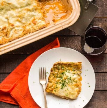 Top view of a corner slice of lasagna bolognese on a white dinner plate with a fork.