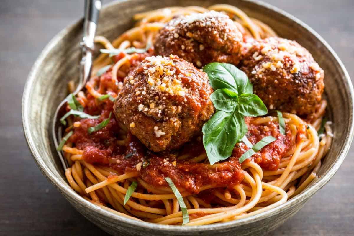 Bowl of meatballs on top of a pile of spaghetti.