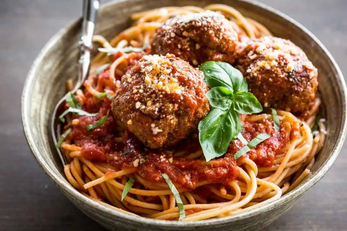 Bowl of meatballs on top of a pile of spaghetti.