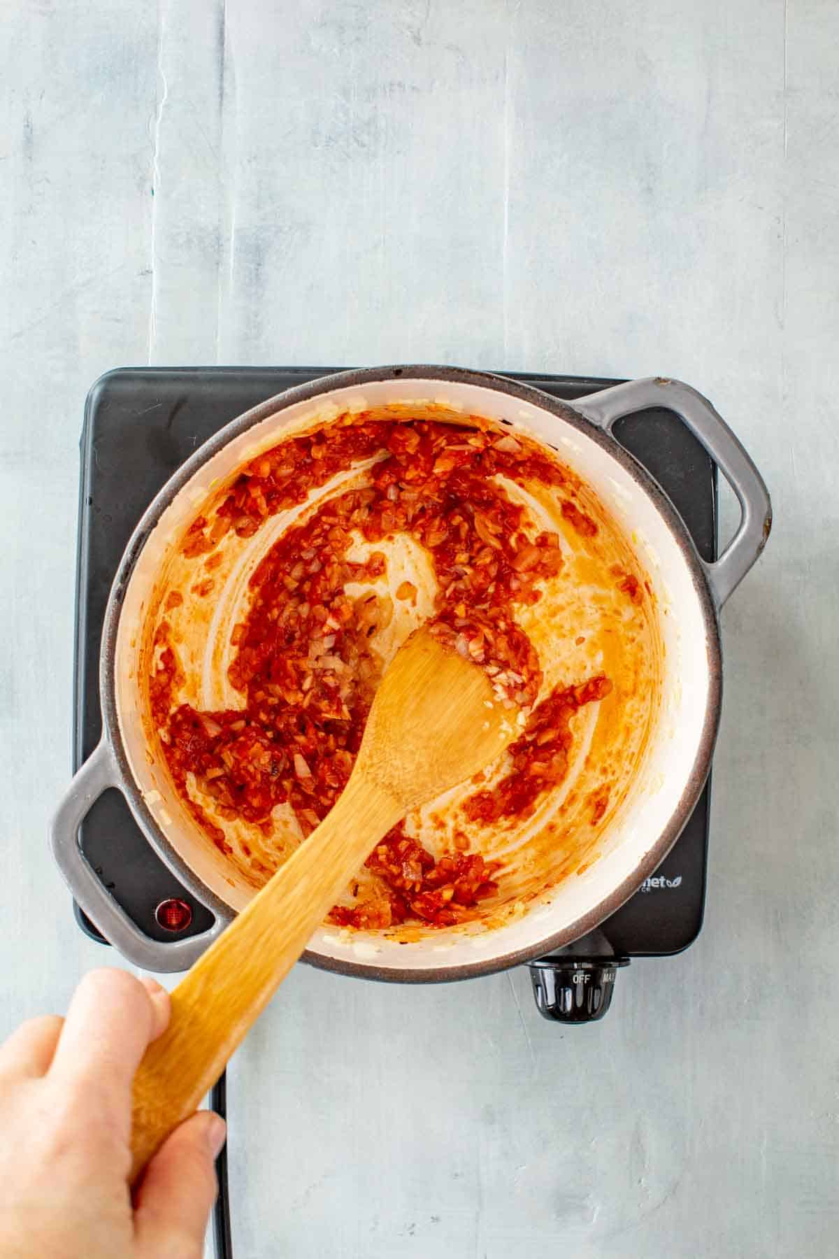 A wooden spoon stirring tomato paste into sautéed onions.