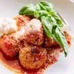 Close up shot of a bowl of meatballs in marinara sauce with a big sprig of basil to garnish.