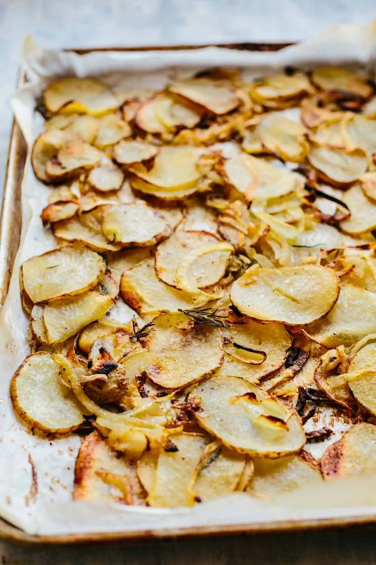 A close up of roasted potatoes and onions on a baking sheet.