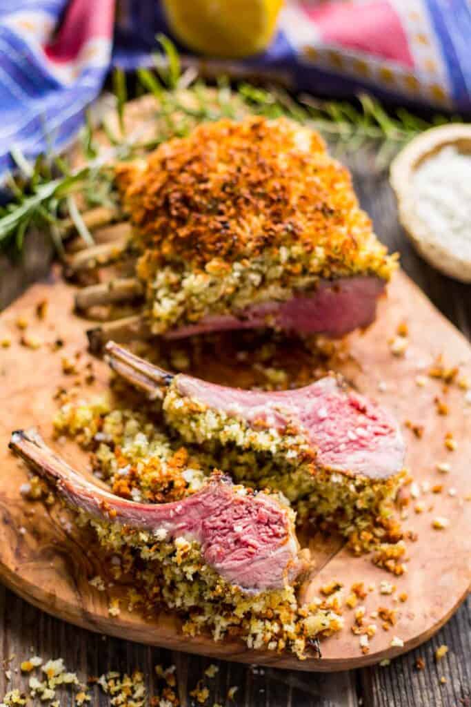 A rack of lamb on a wood cutting board with several chops cut off.