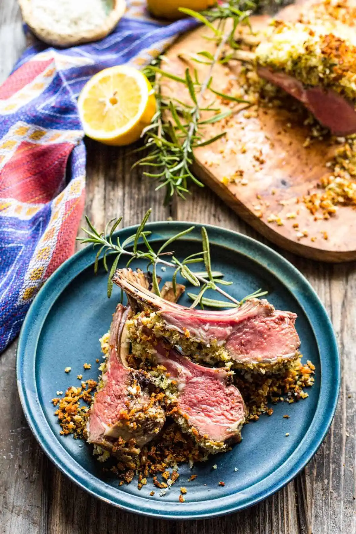 Top view of three Dijon crusted lamb chops set on a blue dinner plate with a sprig of fresh rosemary.