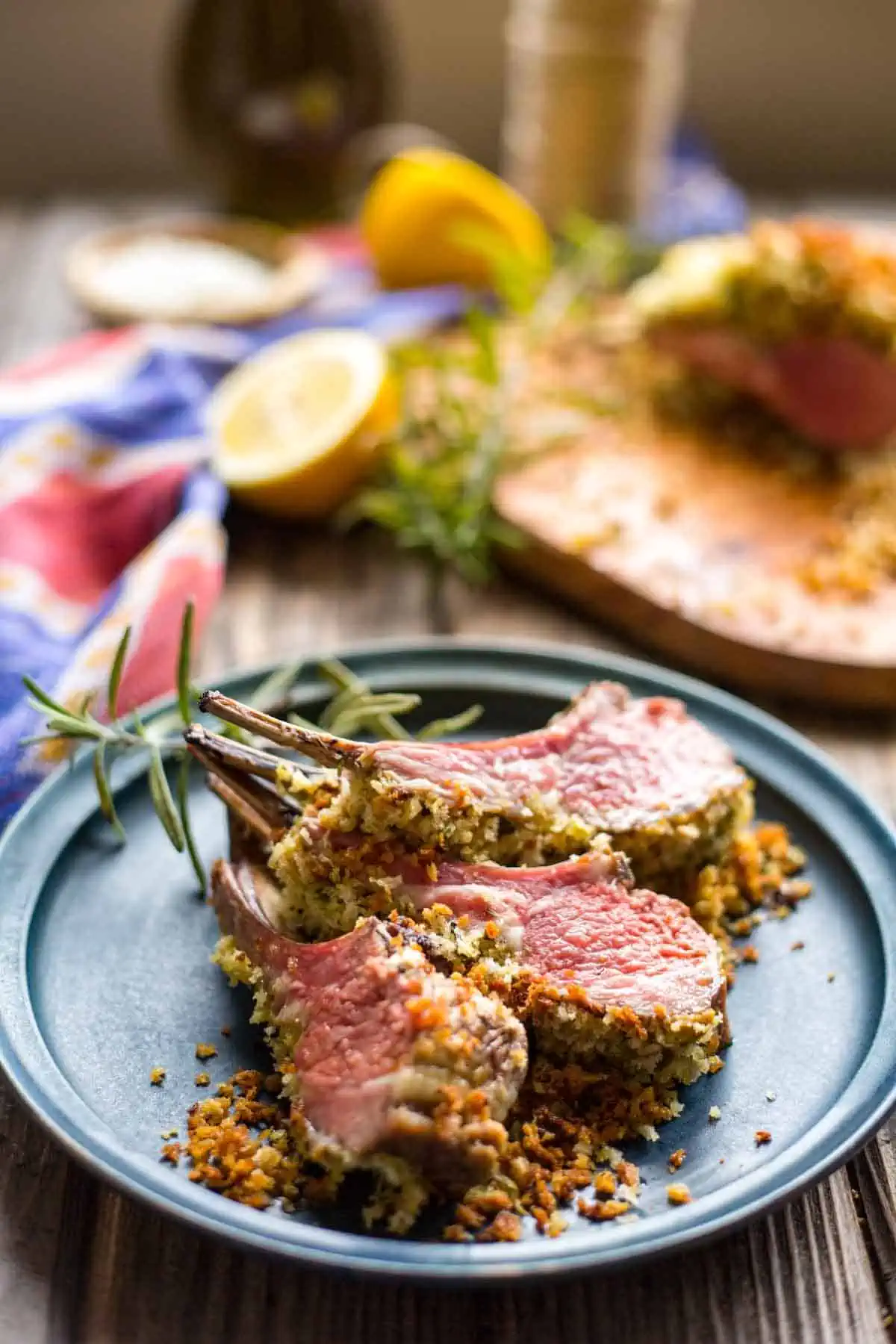 DIjon and herb crusted lamb chops on a blue plate with a sprig of rosemary.