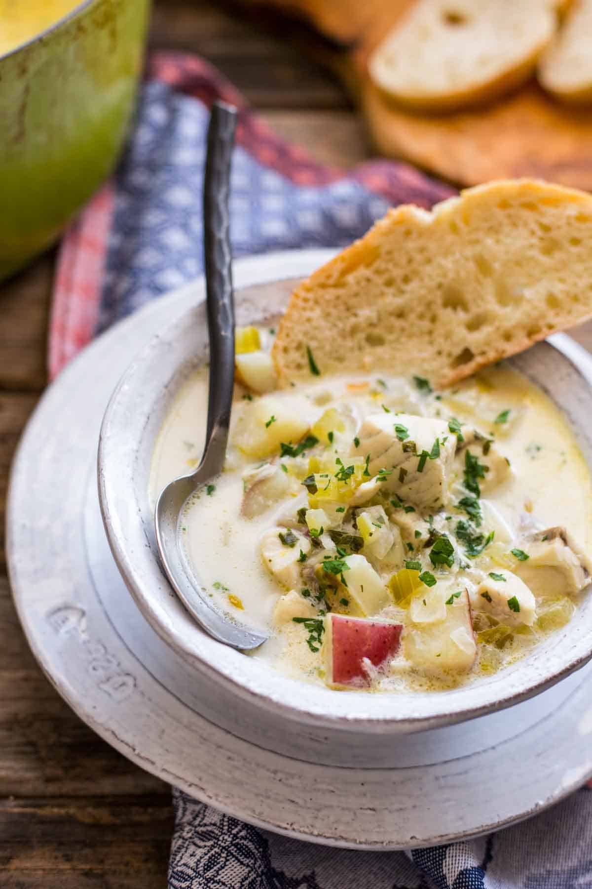 A bowl of creamy chowder with a spoon and a piece of bread. 