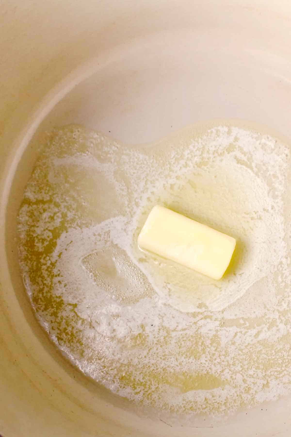 A stick of butter melting in a large Dutch oven.