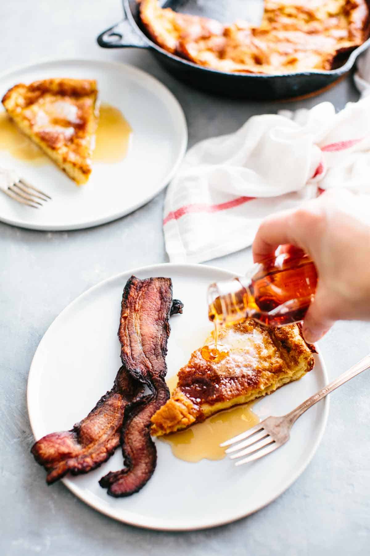 Pouring syrup on a slice of oatmeal Dutch Baby Pancake with bacon.