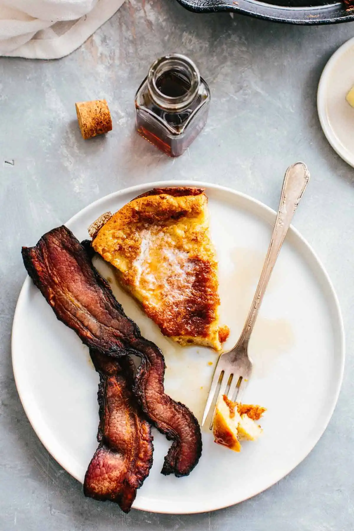 A slice of German pancake with a fork and bacon.