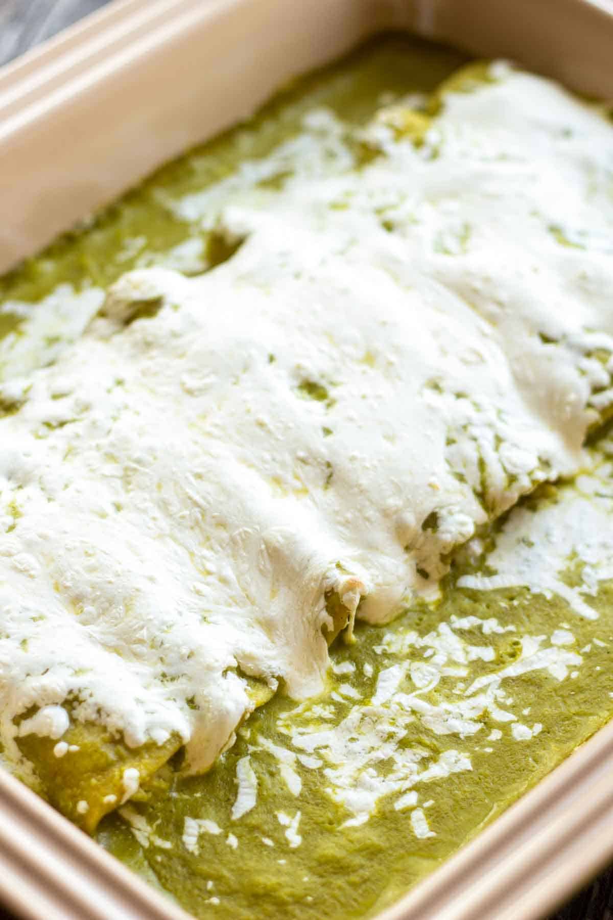 Close up of a tray of enchiladas Suizas verdes with melted cheese on top.