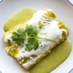 Close up overhead view of two enchiladas with green sauce, cheese and cilantro.