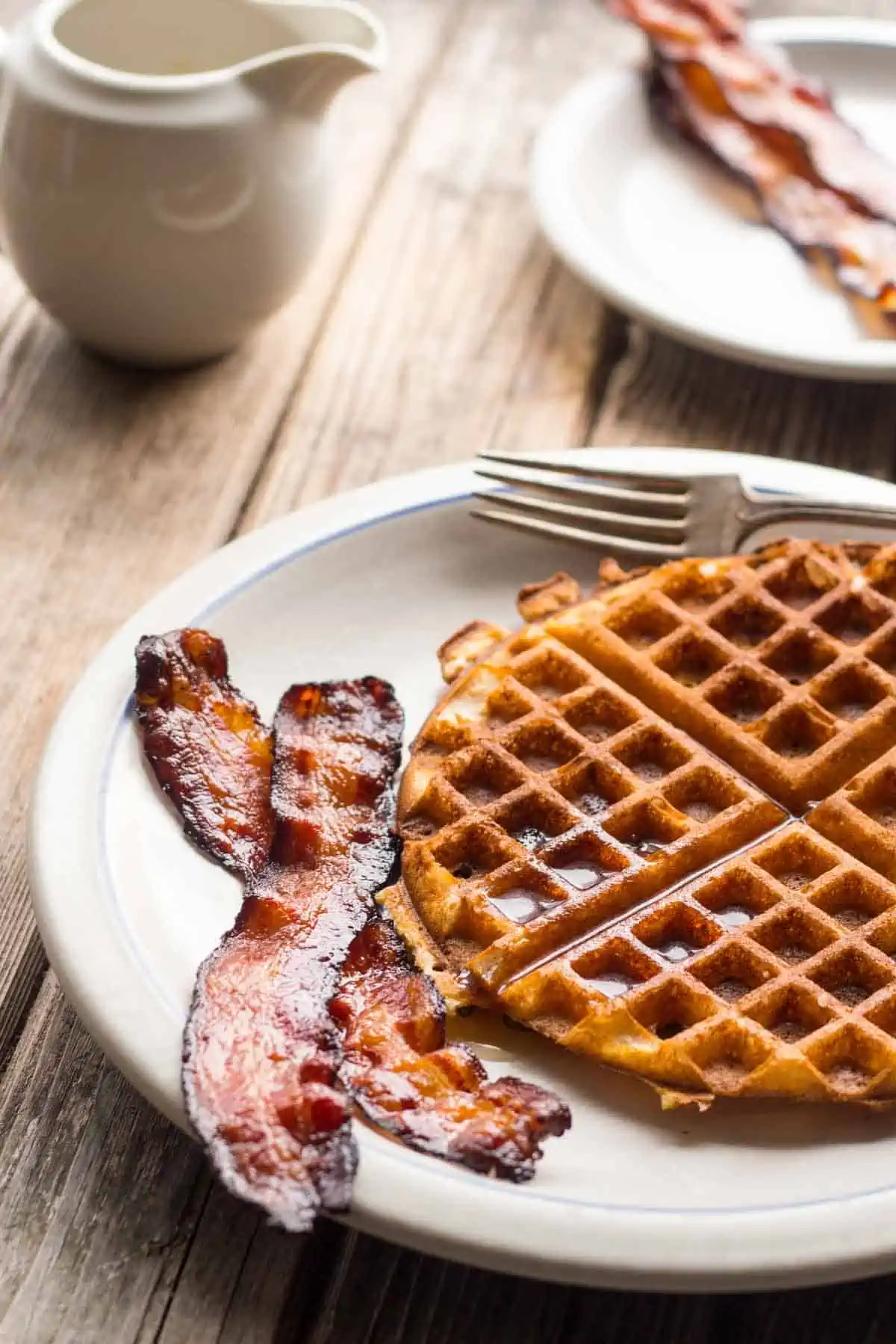 A plate with a waffle and two strips of bacon.