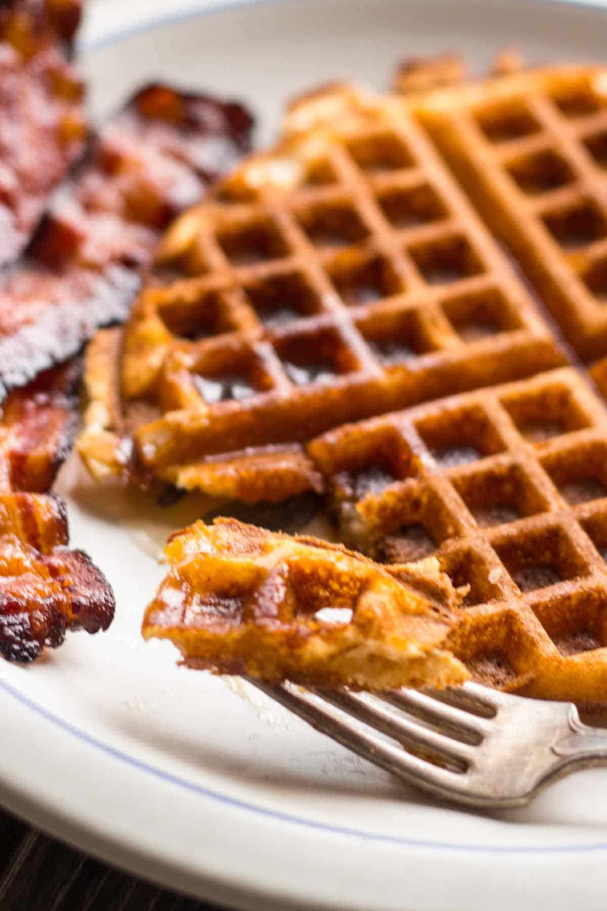A close up of a fork with a bite of waffle on it.