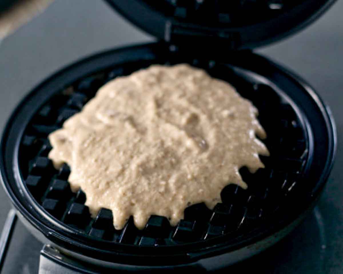 An open waffle iron with raw batter in it.