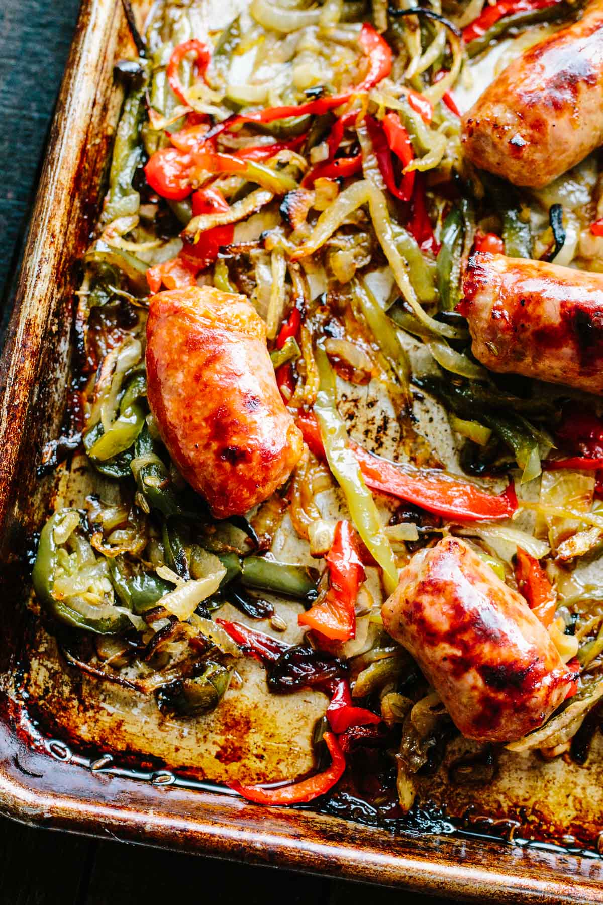 A close up of Italian sausage, peppers and onions on a sheet pan.