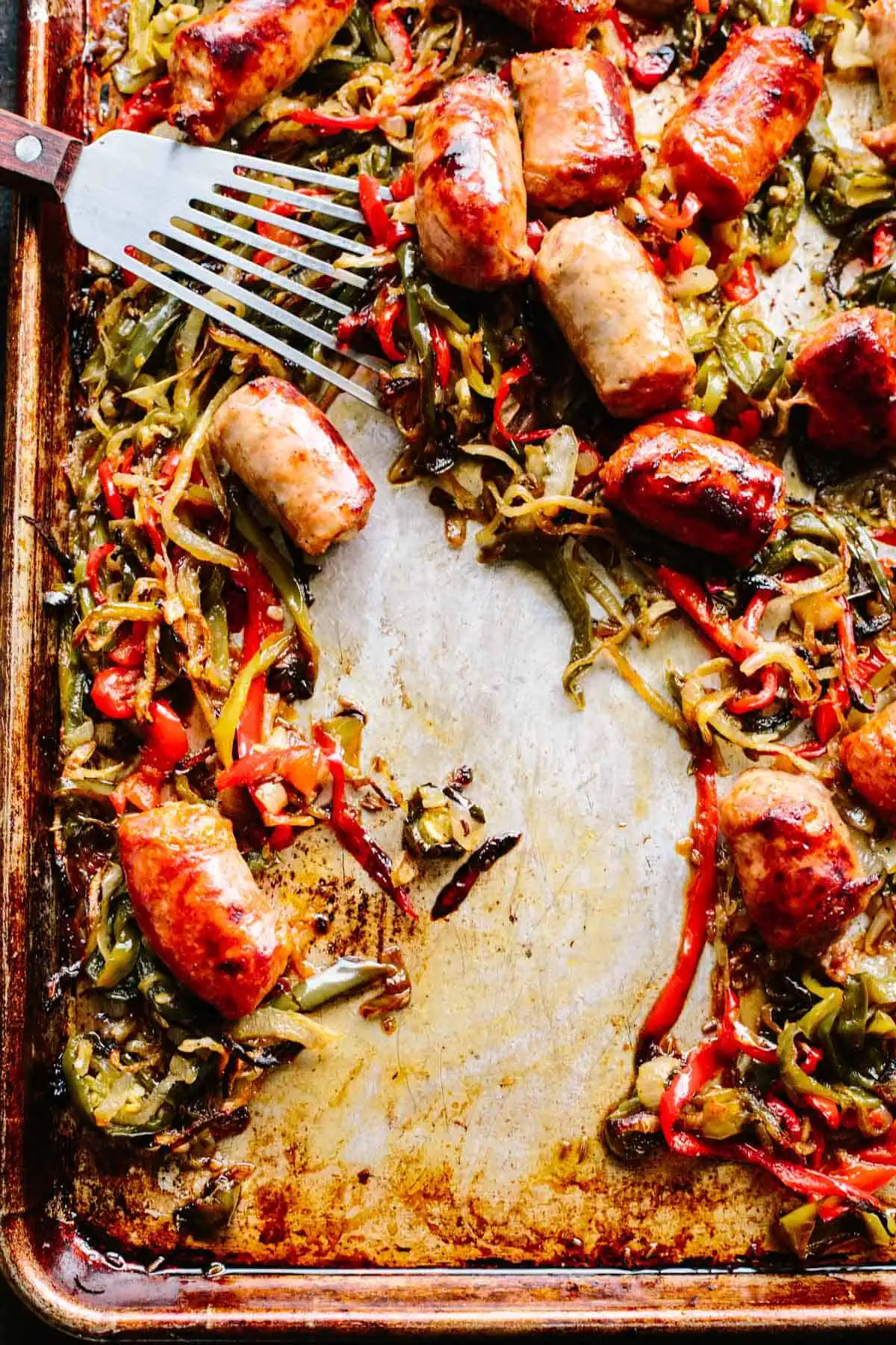 A baking sheet with Italian sausage, peppers and onions and a spatula with an empty spot in the center.