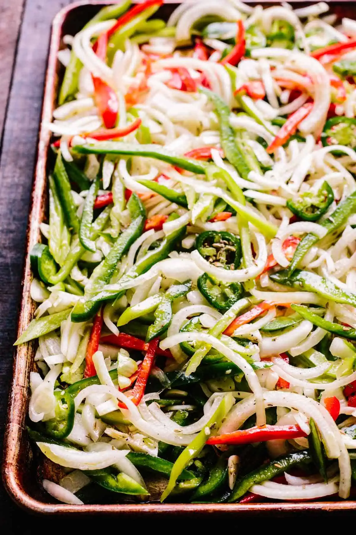 A sheet pan with sliced raw green and red peppers and white onions.