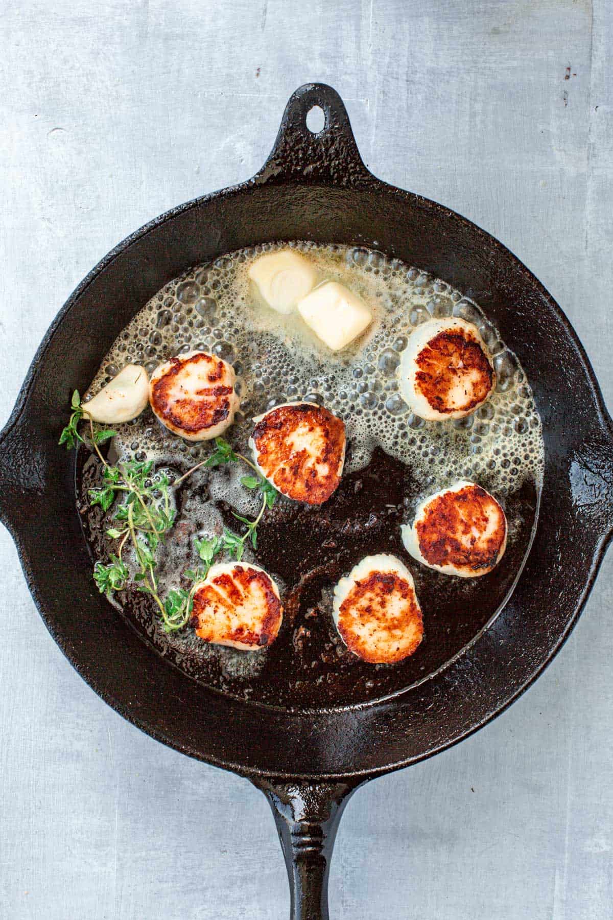 Melting butter in a cast iron skillet with seared scallops, a garlic clove and fresh thyme.