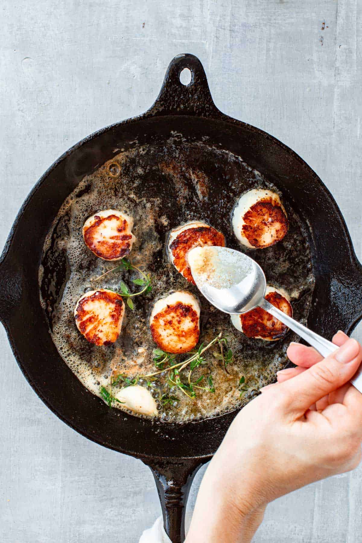 Butter basting seared scallops in a pan with garlic and herbs.