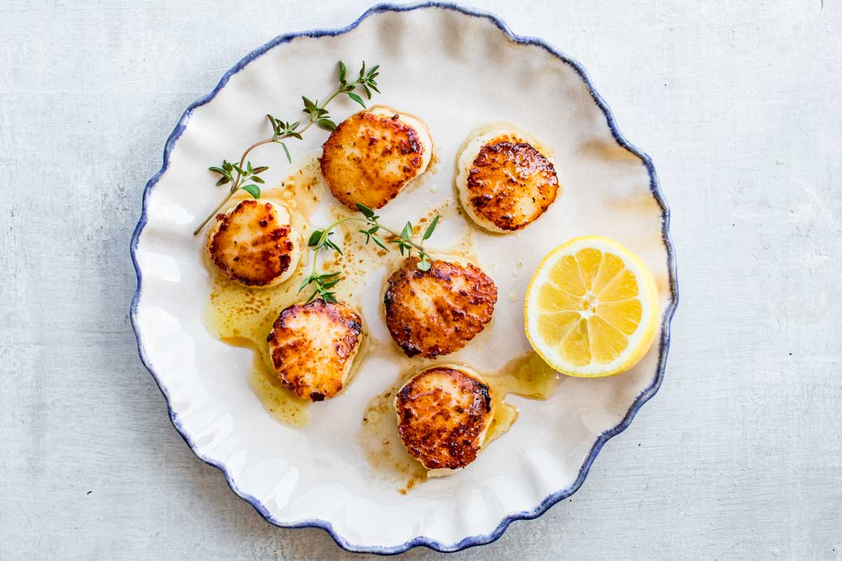 Pan seared scallops with browned butter, thyme and lemon on a white plate.