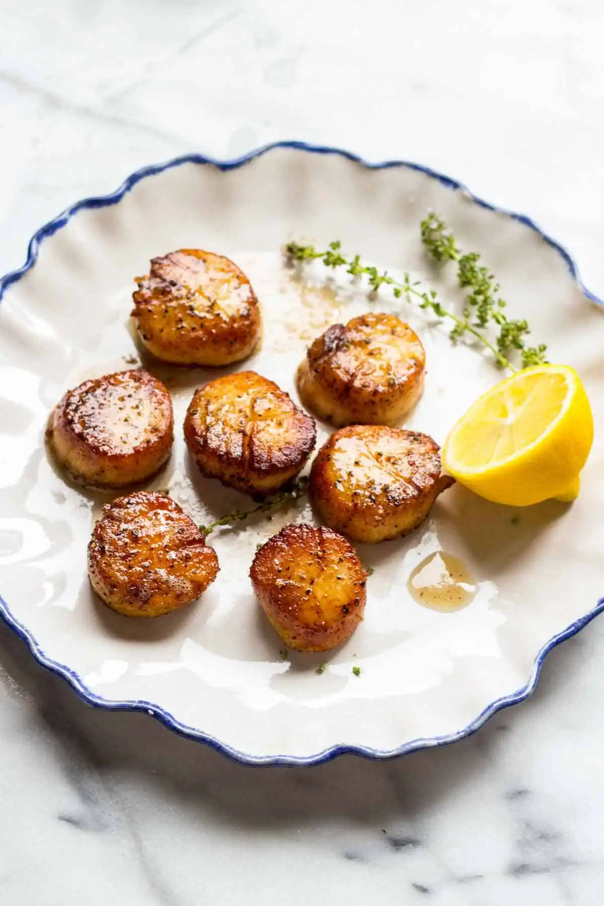 Overhead shot of a plate of seared scallops with half a lemon. 