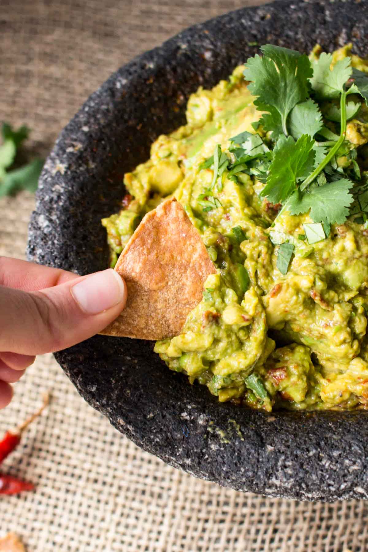 Fingers holding a tortilla chip dipping into a bowl of guacamole.