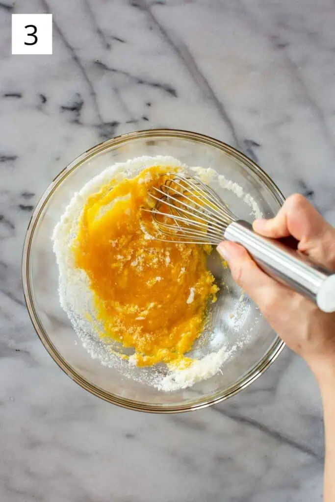A hand whisking together eggs and grated cheese in a bowl.