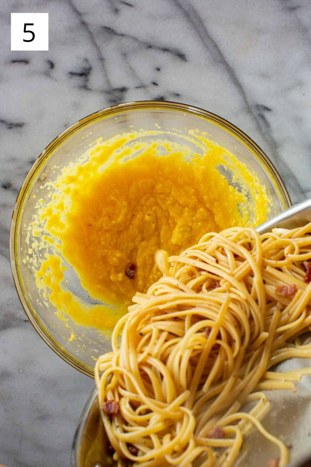 Pasta being poured into a bowl with whisked eggs.