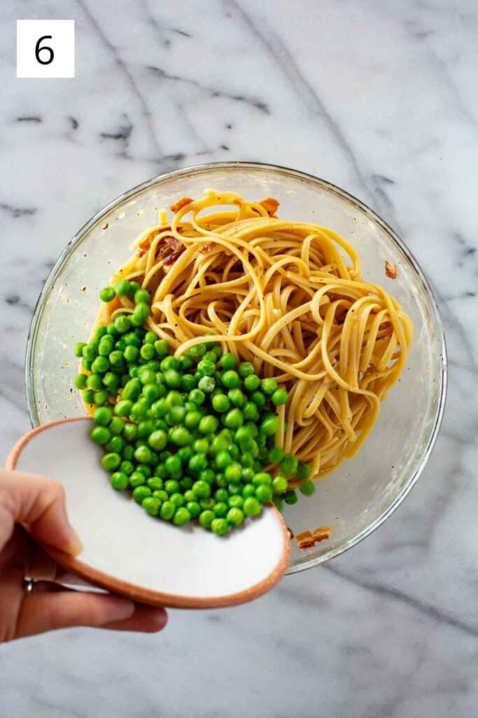 A hand pouring fresh peas into a bowl of pasta.