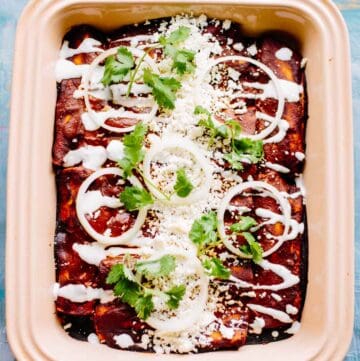 Close up of stoneware baking dish filled with baked chicken mole enchiladas topped with sour cream and cilantro.