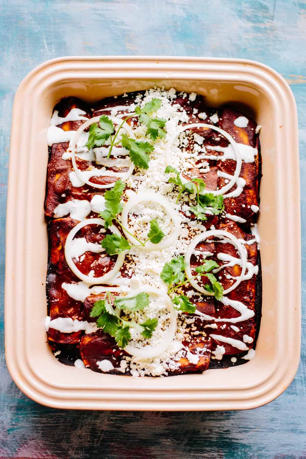 Close up of stoneware baking dish filled with baked chicken mole enchiladas topped with sour cream and cilantro.