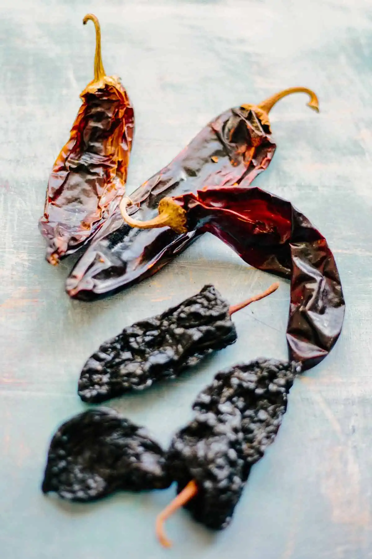Dried ancho chiles and pasilla chiles on a blue background.