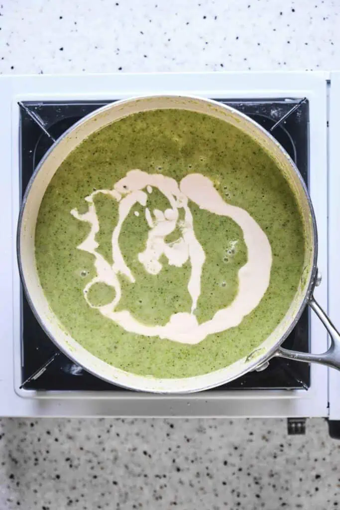 Cream drizzled in a pot of broccoli soup.