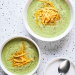 Top view of two bowls of broccoli soup with grated orange cheddar on top.
