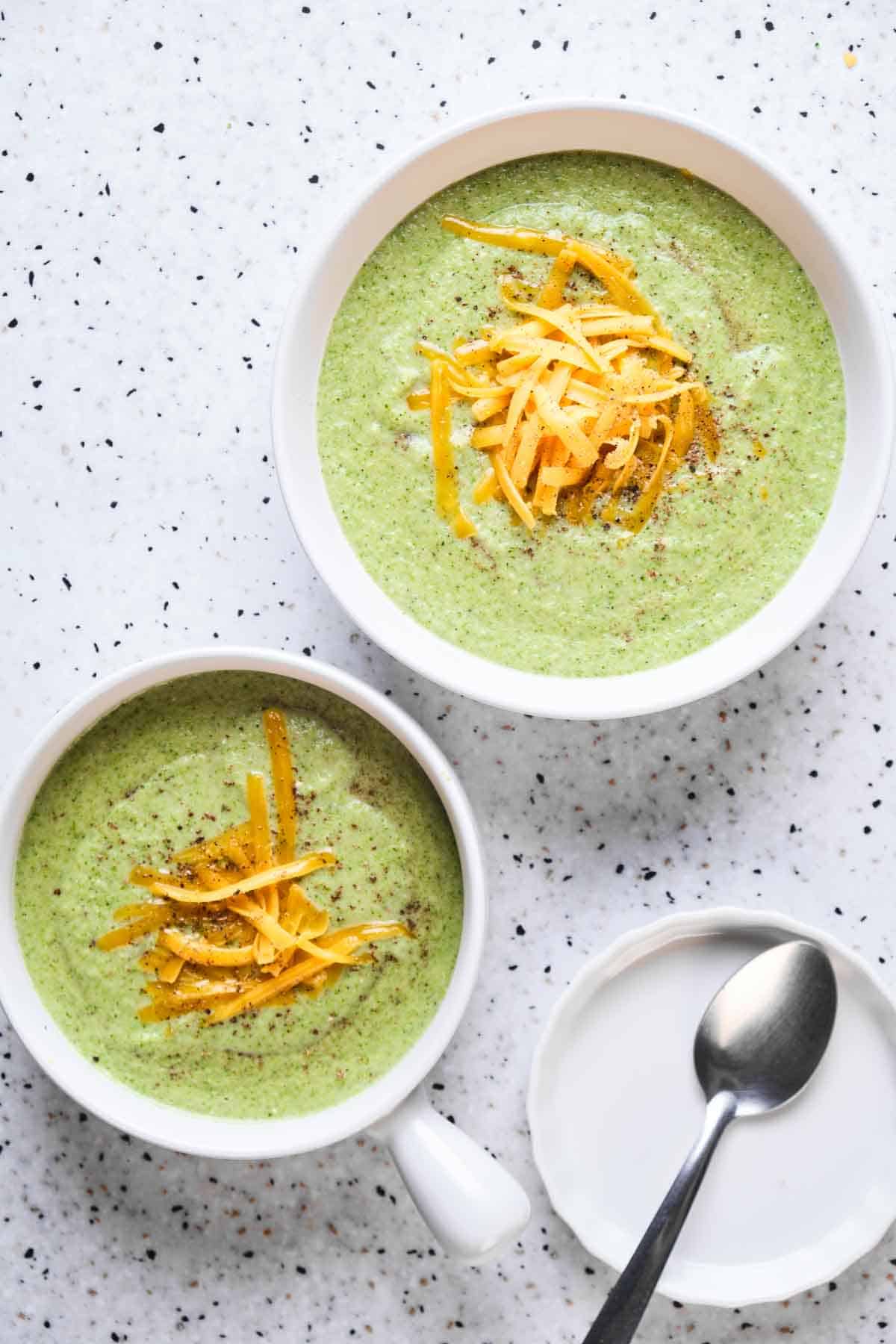 Top view of two bowls of broccoli soup with grated orange cheddar on top.