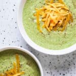 Close up overhead shot of two bowls of cream of broccoli soup with orange cheddar cheese on top.