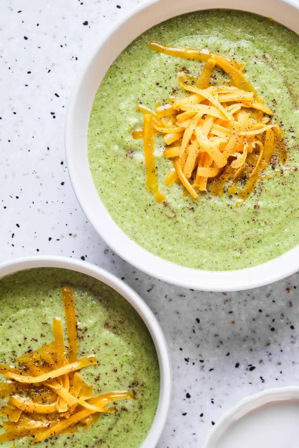 Close up overhead shot of two bowls of cream of broccoli soup with orange cheddar cheese on top.