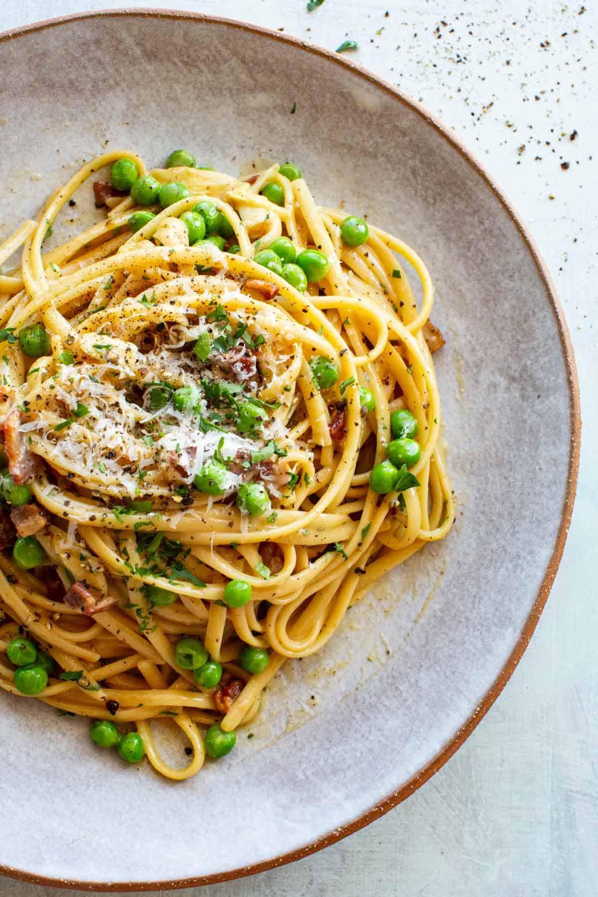 Close up overhead shot of pasta alla Carbonara with peas in a gray stoneware plate.